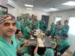 A photo of Tamer Hidari with other nurses wearing green scrubs and hats gathered around a table with a cake at the Nazareth Hospital.